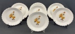Sete pratos rasos em porcelana branca, esmaltado com rosas ao centro, detalhes em relevo e bordas onduladas. Medindo: 25 cm. Um com bicado.