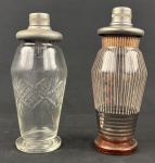 Par de coqueteleiras vintage em vidro sendo uma com decoração geométrica lapidada e outra com decoração em filetes verticais, faixas horizontais e detalhes coloridos, ambas com tampas metálicas. Apresentam sinais de uso e do tempo. Décadas de 19401960. Medindo: 23 e 24 cm.