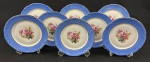 Schmidt. Oito pratos para sobremesa em porcelana nacional, esmaltado e policromado, decoração em relevo, borda azul e medalhão central de flores. Manufatura no verso. Medindo: 18 cm. 2 com bicados e um com fio de cabelo.