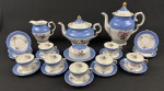 Schmidt. Conjunto para chá e café em porcelana nacional, esmaltado e policromado, decoração em relevo, borda azul e medalhão central de flores. Manufatura no verso. Medindo: Bule  de café 23x22 / bule de chá 15x24 ( desgaste na douração e leve bicado) / leiteira 12x14 (desgastes) / Manteigueira 7x15 (bicado) 7 xícaras café (2 com fio).  12 pires (3 com avaria).