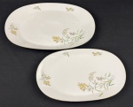 Rosenthal, Germany. Duas travessas em porcelana alemã esmaltada na cor branca delicados ramos floridos e folhagens, finalizados por fino filetes em ouro. Manufatura no verso. Medindo: 23 x 38 cm e 26 x 43 cm.