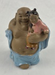 CHINA. Estatueta moldada em cerâmica chinesa representando `BUDA MAITREYA COM CRIANÇA`, vestimentas esmaltadas nas cores azul e rosa. Marcado CHINA. Alt. 19 x 13 cm.
