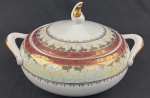 Schmidt. Sopeira em porcelana branca, com larga faixa furta-cor, borda em tom vinho e profusa ornamentação dourada. Manufatura no verso. Medidas: 19 x 32 cm