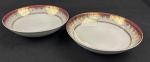 Schmidt. Duas saladeiras em porcelana branca, com larga faixa furta-cor, borda em tom vinho e profusa ornamentação dourada. Manufatura no verso. Medidas: 6 x 25 cm.