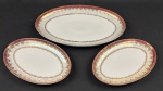 Schmidt. Três travessas em porcelana branca, com larga faixa furta-cor, borda em tom vinho e profusa ornamentação dourada. Manufatura no verso. Medidas:18 x 29 cm e 27 x 42 cm.