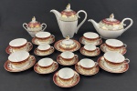 Schmidt. Serviço para chá e café em porcelana branca, com larga faixa furta-cor, borda em tom vinho e profusa ornamentação dourada. Composto de bule de chá, bule de café, açucareiro, manteigueira, seis xícaras para chá com seus pires e seis xícaras para café com seus pires. Manufatura no verso. Medidas: 23 x 24 cm, 17 x 30 cm, 14 x 16 cm, 7,5 x 16 cm. Tampa da manteigueira colada.