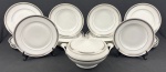MAUÁ. Conjunto em porcelana branca, com decoração em faixa geométrica de gregas, realçada por frisos em tons prateado, composta por 9 pratos rasos, 11 pratos fundos e 1 sopeira com tampa. Total: 21 peças. Marca do fabricante na base. Medidas: pratos rasos 24 cm de diâmetro; pratos fundos 4 x 23 cm; sopeira 16 x 27 cm.