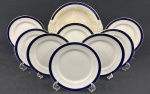 Thomas Hughes & Son Ltd, Staffordshire, Inglaterra - Selo `Unicorn Trade Mark`, c. 1910–1930. Conjunto para sobremesa em faiança Inglesa, esmaltado na cor branca e decorado com filetes duplos em azul-cobalto nas bordas Padrão Bleu Mazarine / Blue de Roi. Composto de prato para bolo e 8 pratos para sobremesa. Manufatura no verso. Medindo: 26 cm e 18 cm. Craquelê. Prato para bolo e 2 de sobremesa com manchas.