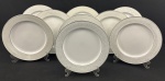 Schmidt, Voyage. Nove pratos rasos em porcelana esmaltada na cor branca, borda decorada e filetes em prata. Manufatura no verso. Medindo: 25,5 cm.