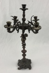 Candelabro antigo em bronze para cinco velas, apresentando uma figura de anjo na haste central e detalhes de arabescos. Medindo: 50 x 31 cm.
