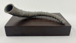 Chifre decorativo em bronze, apresentado sobre base em madeira. A peça possui formato curvo com anéis em relevo ao longo do corpo e acabamento com pátina natural. Medindo: 12 x 26 x 18 cm conjunto, 8 x 29 cm chifre, 5 x 28 x 18 cm caixa