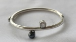 Pulseira rígida em prata de lei, roliça e adornada com hematita redonda e zircônia. Medindo: 50 mm de diâmetro. Peso: 16,1 g.