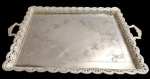 Grande e imponente bandeja retangular em metal espessurado a prata, com centro gravado por motivos de volutas e arabescos, borda recortada, vazada e ricamente lavrada, ladeada por duas alças. Medindo: 5 x 72 x 48 cm.