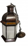 Lanterna pendente em metal patinado, de formato sextavado, com painéis em vidro fosco e detalhes em vidro colorido, encimada por cúpula facetada com respiros vazados. Acompanha corrente e canopla para fixação. Medindo: 40 x 24 cm; altura total com a corrente: 94 cm.