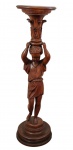 Coluna pedestal em madeira entalhada, com fuste escultórico, representando jovem sustentando capitel ornamentado por volutas e folhagens. Tampo e base circulares moldurados.  Medindo: 100 x 27 cm.