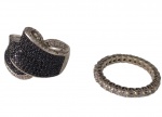 Dois anéis em prata, sendo um de aro largo, com desenho sinuoso e cravejamento de pedras negras e incolores, e outro tipo aliança, inteiramente cravejado por zircônias de lapidação circular. Aros: 22 e 19. Peso total: 10,9 g.
