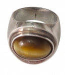Anel masculino em prata, de aro largo, ornamentado por pedra olho-de-tigre de formato oval e lapidação cabochão, com característico efeito de chatoyance. Laterais com acabamento texturizado. Aro: 22. Peso: 11,5 g.