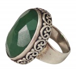 Grande anel em prata, ornamentado por pedra verde de formato oval e lapidação facetada, emoldurada por friso lavrado com motivos de volutas. Aro: 17. Peso: 14,4 g.