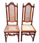 Duas antigas cadeiras em madeira maciça, com espaldar alto, colunas torneadas, ornamentos entalhados com motivos florais e assentos e centros dos espaldares em palhinha sintética. Uma das cadeiras apresenta avarias e necessita de restauração. Medindo: 116 x 43 x 46 cm, cada. 