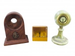 RELÓGIO, três (3) peças, sendo: A) um (1) suporte de mesa em madeira, com abertura circular e aplique metálico representando âncora marinha, medindo 11,5x9x5cm, B) um (1) relógio despertador da marca EUROPA, com caixa quadrangular em material sintético amarelo, medindo 6x6,5x6cm e C) um (1) relógio de mesa em mármore esverdeado, corpo torneado e colado, mostrador dourado, quartz, algarimos romanos com sinais de oxidação, medindo 12x5,5cm.