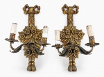 LUMINÁRIAS, par (2) de arandelas confeccionadas em madeira entalhada a mão por flores e folhagens encimado por laçarote, hastes em metal dourado, bocais revestidos em madeira representando vela, sinais de fita e falhas na douração, medindo 44x23cm. Vendido no estado da foto, leves mossas e oxidações na haste.