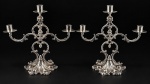 METAL PRATEADO, par (2) de candelabros para três velas confeccionados em metal espessurado a prata, hastes curvas em arabescos recortados e vazados, base cinzelada em pétalas com elementos relevados, 1 bobeche com mossa, medindo 29,5x33cm.