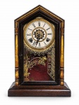 RELÓGIO, um (1) relógio de mesa ou parede, com caixa em madeira de formato arquitetônico, remate superior em frontão, colunas laterais torneadas e detalhes dourados. Mostrador circular com algarismos romanos, dois furos para corda e centro vazado com parte do mecanismo aparente. Porta frontal em vidro decorado com motivos florais e geométricos dourados. Funcionando, sem garantias futuras, falhas no mostrador, acompanha pêndulo e 2 chaves, medindo 43x24x10cm.