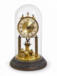 RELÓGIO, um (1) antigo relógio de mesa alemão tipo aniversário / 400 dias, com mecanismo mecânico de torção, estrutura em metal dourado, mostrador com algarismos arábicos e pêndulo giratório com quatro esferas (corda arrebentada). Protegido por redoma de vidro sobre base circular escura. Movimento marcado Germany, com inscrições na máquina. Peça com sinais de uso, oxidação e desgaste compatíveis com a idade. Sem teste de funcionamento. No estado, medindo 30cm de altura.