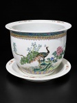 PORCELANA ORIENTAL, um (1) cachepot com presentoir confeccionado em porcelana oriental na tonalidade branca, decorado por pavão e elementos florais em policromia, adornado por nuvens e faixa floral com fundo azul, medindo 17x23,5cm.