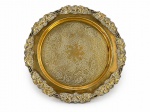 METAL DOURADO, uma (1) bandeja redonda confeccionada em metal dourado, cinzelado por elementos florais e vegetalistas, borda em frutos e folhagens em relevo e recorte, medindo 40cm de diâmetro.