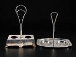 METAL PRATEADO, dois (2) suportes para galhetas, sendo: A) 1 confeccionado em metal espessurado a prata, estilo art noveau, decorado por frisos e elementos relevados, base recortada e alça central em vazados, leves mossas, medindo 26x19x9,5cm e B) 1 confeccionado em aço inox, borda em folhagens e perolados e pega central fixa em vazado, medindo 22x23,5x13cm.