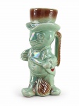 PORCELANA, uma (1) caneca confeccionad em porcelana esmaltada em furtacor, modelada na forma de personagem masculino com cartola, em tom verde com detalhes marrons e policromados, apresentando alça lateral moldada. Possui aplicação promocional com inscrição Festival Refrigerantes Grupo Prata Real  Feliz Natal, Próspero Ano Novo e emblema de coroa no verso. Medindo 18cm de altura.