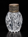 CRISTAL, um (1) perfumeiro confeccionado em cristal translucido com lapidação geométrica e estrelas em baixo relevo, tampa em metal dourado com cinzelado vegetalista e marcas de uso, ausência da tampa interna, medindo 11cm de altura.
