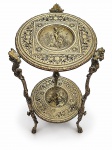 MOBILIÁRIO - MOBILIÁRIO, uma (1) mesa auxiliar de 2 estágios, em bronze, cinzelada ao gosto neoclássico, ricamente ornamentada em relevo com motivos florais, arabescos e figuras angelicais. Estrutura com três pés curvos decorados e dois tampos circulares, ambos trabalhados com cenas figurativas em relevo e cercaduras ornamentais. Medida : 74,5 x 26 cm
