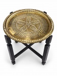 MOBILIÁRIO, uma (1) mesa auxiliar, com estrutura em madeira escurecida, de quatro pés retos unidos por travessas cruzadas, sustentando tampo circular em metal dourado, ricamente trabalhado em relevo com motivos florais e geométricos. Medida : 50 x 46 cm