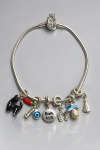 JOIA, uma (1) pulseira PANDORA em PRATA DE LEI, contrastada 925, com fecho decorado e diversos berloques, entre eles elefante, pimenta vermelha, olho grego, medalha com a inscrição Basta ter Fé, ferradura, cogumelo e imagem de Nossa Senhora Aparecida, além de outros elementos decorativos, medindo 29cm de comprimento.