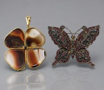 BIJUTERIAS, duas (2) peças, sendo: A) 1 pingente em formato de trevo de 4 folhas, em metal dourado, com quatro placas de ágata de tonalidades distintas, medindo 5x5cm e B) 1 broche em formato de borboleta, em metal escurecido, ricamente incrustado por pedras vermelhas, com ausência de algumas, medindo 4,5x6cm.
