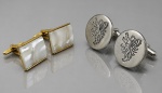 DIVERSOS, dois (2) pares de abotoaduras, sendo: A) 1 confeccionado em metal dourado com incrustação de placa em galalite na tonalidade cinza, sinais de uso, medindo 1,5x2cm e B) 1 em metal prateado com cinzelado de leão rampante, estilo heráldico, medindo 2cm.