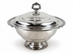 METAL PRATEADO, uma (1) sopeira confeccionada em metal espessurado a prata com banho novo, bojo liso, borda cinzelada em recortes e concheados relevados, pega da tampa em volutas em vazado, medindo 25x32cm.