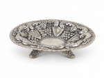METAL BOLIVIANO, uma (1) fruteira circular confeccionada em metal espessurado a prata martelado, cinzelado por frutos, folhagens e arabescos em relevo, borda em ondulações apoiada sobre 3 pés curvos, medindo 6x25cm, banho novo.