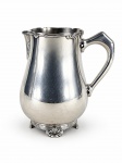 METAL PRATEADO, uma (1) jarra confeccionado em metal espessurado a prata da manufatura FRACALANZA, cinzelada por caneluras e laçarotes com borda em recortes, alça lateral em vazado, banho novo, medindo 19,5x17,5x11,5cm.
