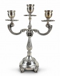 METAL PRATEADO, um (1) candelabro para três velas confeccionado em metal espessurado a prata, corpo torneado, cinzelado por caneluras e folhagens, braços curvos em arabescos, base circular escalonada, apoiada sobre 4 pés curvos, medindo 31x23cm, banho novo.