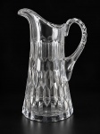 CRISTAL, uma (1) jarra confeccionada em cristal translucido com lapidação de caneluras e dedões em baixo relevo, borda em recorte com alça vazada, apresenta bicados na base, medindo 27x17x9cm.