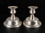 METAL PRATEADO, par (2) de castiçais confeccionados em metal espessurado a prata, borda cinzelada em caneluras, fitas cruzadas, base escalonada com haste torneada, banho novo, necessita polimento, medindo 11cm de altura.