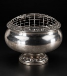 METAL INGLÊS, uma (1) floreira confeccionada em metal espessurado a prata, corpo bojudo, bordas cinzelado por flores e folhagens, grade removível, base circular, banho novo, medindo 16x18cm.