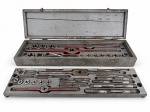 FERRAMENTAS, um (1) conjunto antigo de machos e cossinetes para abertura e recuperação de roscas, confeccionados em aço, com diversas medidas, acompanhado de porta-machos, porta-cossinetes e acessórios, acondicionado em estojo metálico com encaixes individuais. Apresenta sinais de uso, oxidação, manchas e desgastes compatíveis com a idade. Conteúdo não conferido quanto à completude. Peças no estado, caixa medindo 10x77,5x21cm.