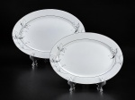 PORCELANA DM BRASIL, duas (2) travessas ovais confeccionadas em porcelana na tonalidade branca, decorada por flores e folhagens em monocromia na tonalidade cinza com filetes e realces em prata, leves falhas na prateação, medindo 35x24cm e 30x21cm.
