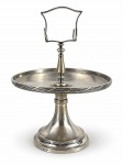 METAL PRATEADO, uma (1) fruteira confeccionada em metal espessurado a prata, bordas cinzeladas em caneluras e fitas cruzadas, base cônica e escalonada, haste central torneada com pega vazada e ganchos laterais, peça monogramada CS, vestígios da marca, vide foto, apresenta falhas na prateação, medindo 34,5x26,5cm, apresenta mossa no prato.
