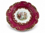 PORCELANA VISTA ALEGRE, um (1) prato medalhão confeccionado em porcelana portuguesa na tonalidade branca, borda esmaltada em tom vinho com realces vegetalistas em relevo, recortes e filetados em ouro, decorado por elementos geométricos e centro com cena ninfa em policromia, apresenta falhas na douração, medindo 6x36,5cm.