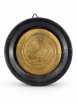 QUADRO, um (1) adorno de parede com medalhão central em metal dourado trabalhado e cena em relevo alusiva ao Café do Brasil, apresentando figura feminina e personagem rural em composição campestre. Moldura circular com forração em couro, medindo 14,5cm.